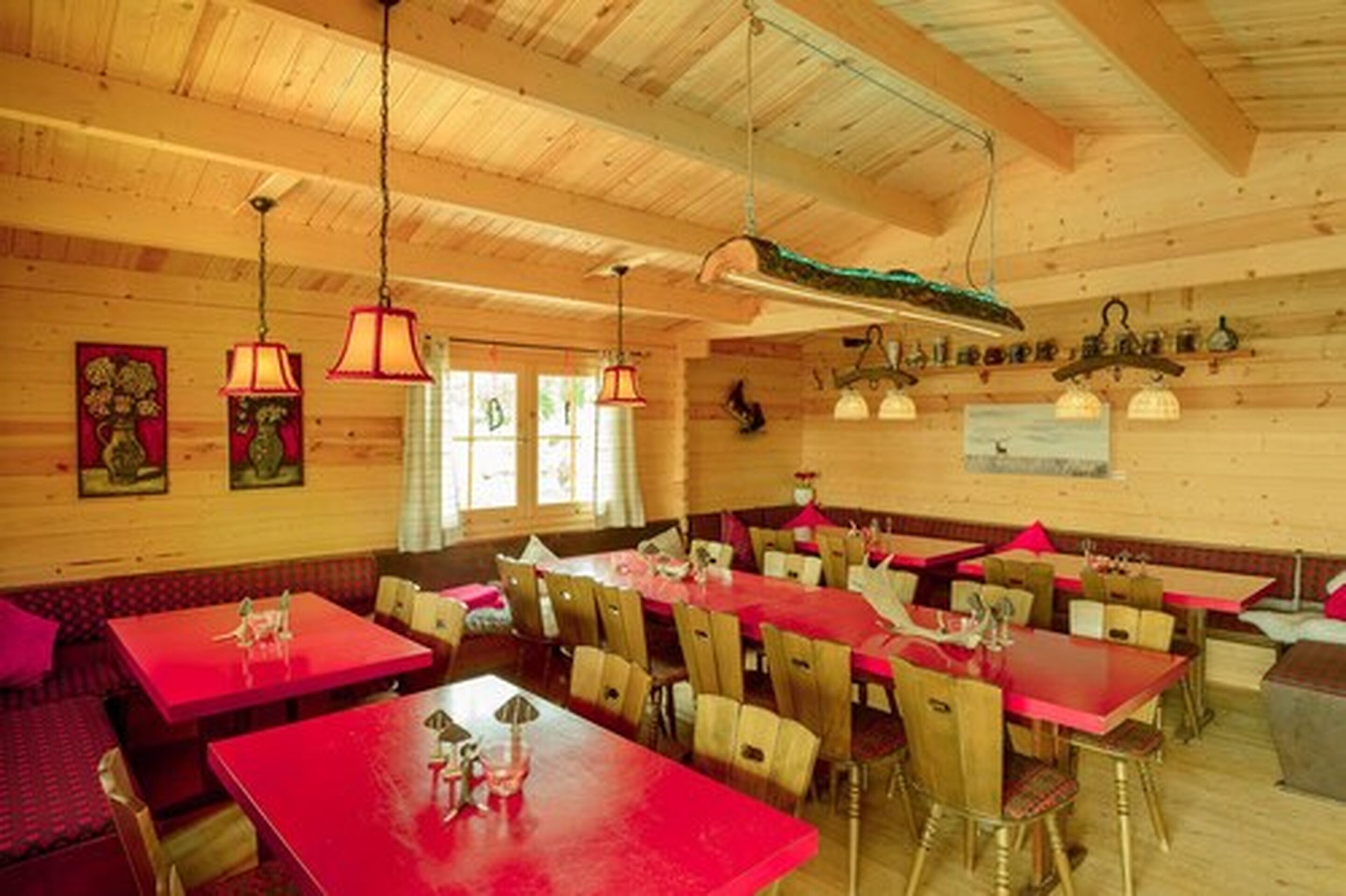 A restaurant with wooden walls and ceiling, red tables and chairs, and hanging lamps.
