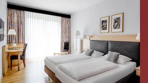 Habitación de hotel con cama doble, escritorio con silla, lámpara y dos cuadros en la pared.
