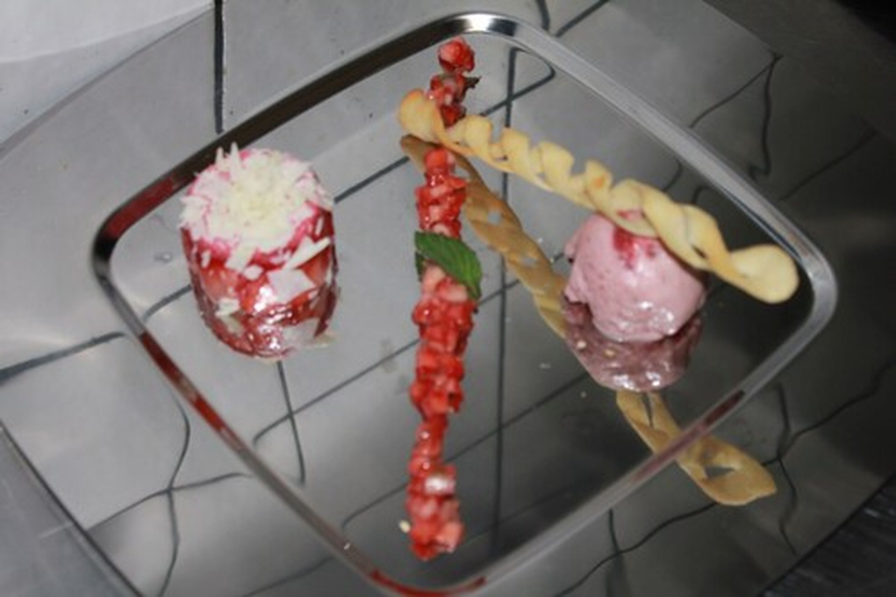 Un plateau de desserts comprenant divers éléments, notamment un dessert rouge et blanc, un dessert enrobé de chocolat et un dessert surmonté d’une garniture jaune.