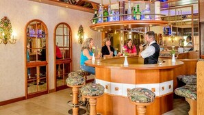 Zona de bar con barra circular, taburetes y un cantinero. Hay dos puertas con paneles de vidrio y un candelabro.