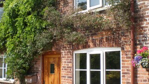 A brick house with a wooden door, two windows, and potted plants in front. - Farmhouse Cottage Sleeps 2 (1 en-suite Bedroom) (Congleton)