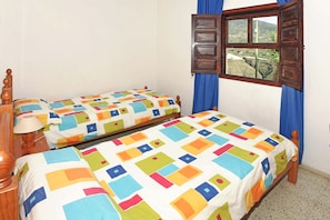 Une chambre avec deux lits simples, une tête de lit en bois, une fenêtre avec des rideaux et une vue sur l’extérieur.