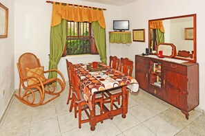 A dining area with a table set for four, a rocking chair, a wooden cabinet with a mirror, and a television on a stand. - Casa Amagar en Tijarafe (Tijarafe)