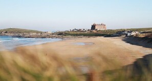 A coastal landscape with a sandy beach, a large building on a hill, and a lighthouse in the distance.