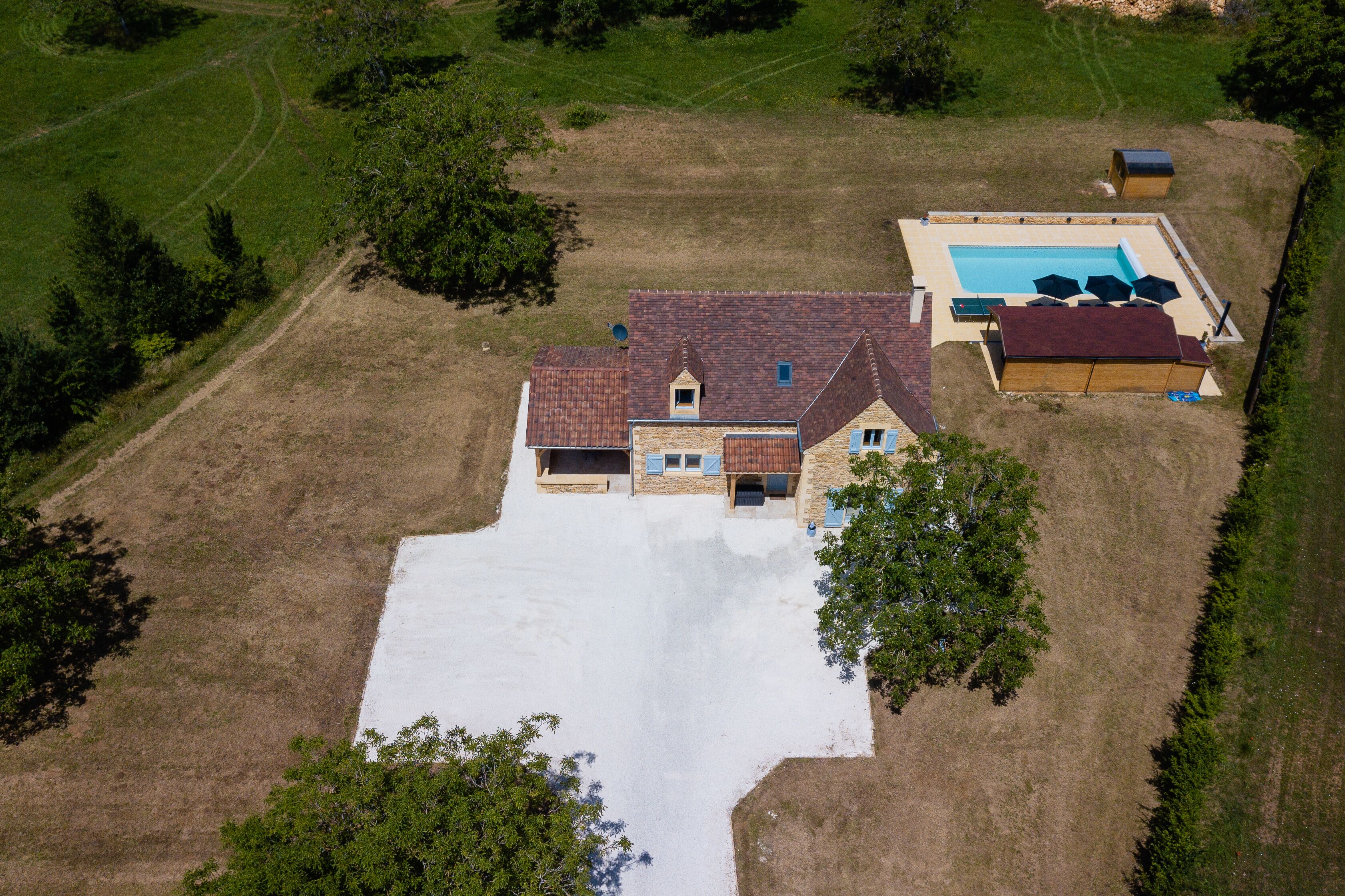 An aerial view of a house with a swimming pool, a covered patio, and a large open driveway.