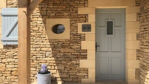 Un edificio de piedra con una puerta azul, un letrero que dice "MAISON MARRON" y una planta en maceta con flores moradas.