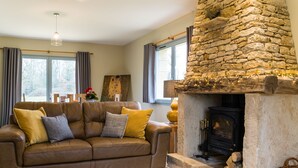 Una sala de estar acogedora con chimenea de piedra, un sofá de cuero y un amplio ventanal con cortinas.