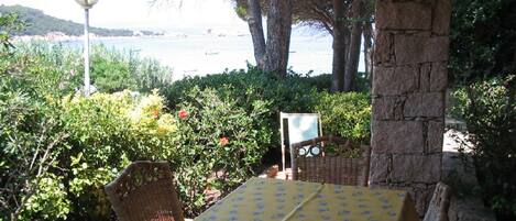 Mesa exterior con mantel amarillo, sillas de mimbre y vista al mar.
