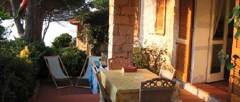 An outdoor patio with a table and chairs, stone walls, and wooden shutters.