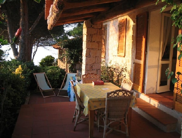 An outdoor patio with a table and chairs, stone walls, and wooden shutters. - APARTMENT FOR SEA FRONT WITH TERRACE (Baja Sardinia)