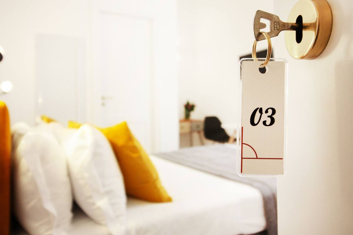 A hotel room with a bed, a key tag, and a door in the background.