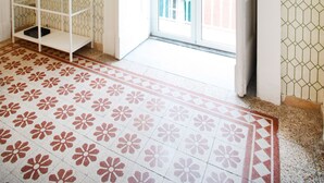 A room with a patterned floor, a white shelf with a vase, and a view of a building through an open door. - Le Quinte del Bellini (Naples)