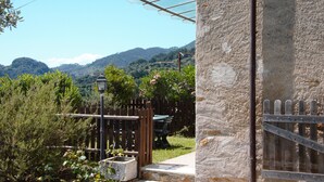 A stone building with a wooden gate, a metal fence, and a view of green hills in the background. - Villa with private pool, 5 minutes drive from the beach of Forte dei Marmi. (Ripa di Seravezza Lucca)
