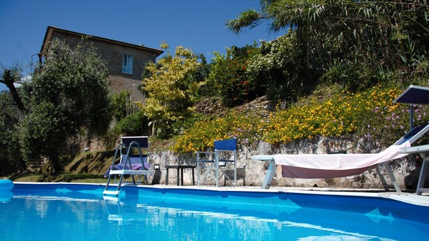 A swimming pool with a diving board, lounge chairs, and a stone wall with flowers. - Villa with private pool, 5 minutes drive from the beach of Forte dei Marmi. (Ripa di Seravezza Lucca)