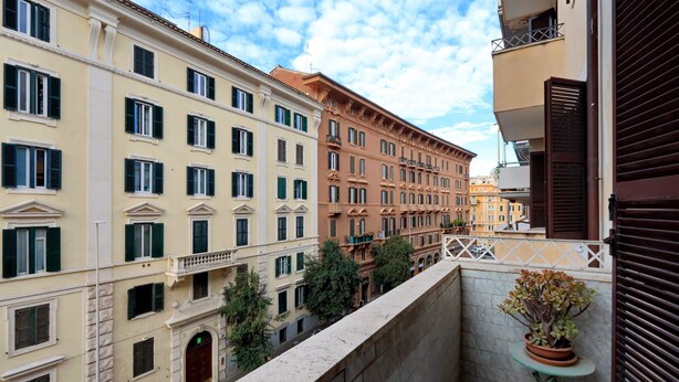 A narrow urban street with multi-story buildings, a small balcony with a potted plant, and a clear sky. - Casa dell'Artista Roma (Rome)