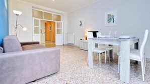 A modern living room with a sofa, a dining table set for two, and a large window. - Casa dell'Artista Roma (Rome)