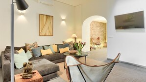A modern living room with a grey sofa, a wooden coffee table, and a chair. There is a TV mounted on the wall and a lamp on a floor stand. - Stylish townhouse with large pool, central Pollensa (Pollensa / Pollença)