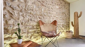A room with a stone wall, a cactus sculpture, a wooden table with a plant, and a modern chair. - Stylish townhouse with large pool, central Pollensa (Pollensa / Pollença)