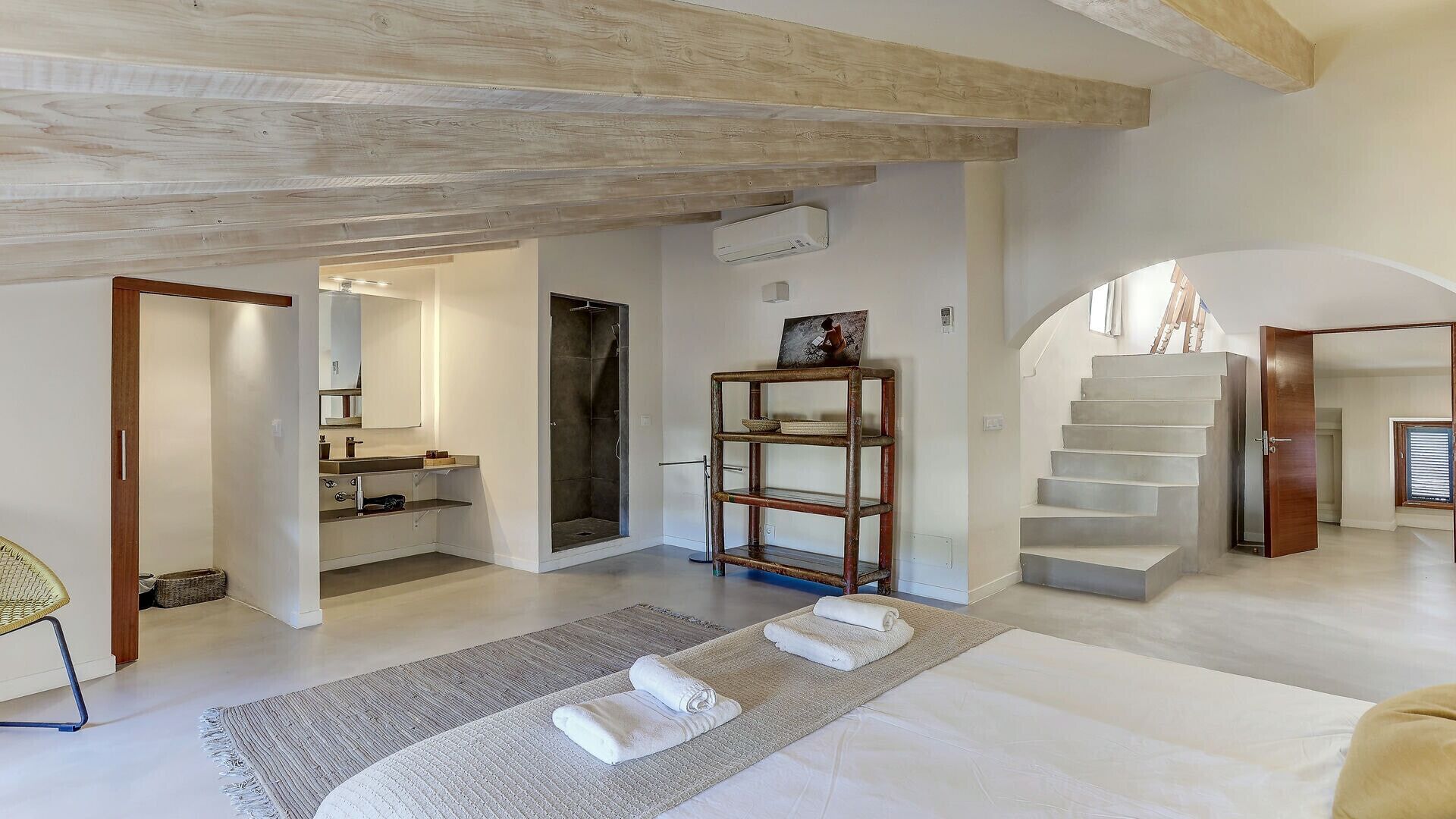 Ein großzügiger Wohnbereich mit einem großen Bett, einer hölzernen Bank und einer Treppe zu einer oberen Ebene.