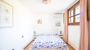 Ein Schlafzimmer mit einem Bett, einem Nachttisch, einer Wand-Klimaanlage und einem Fenster mit Vorhängen.
