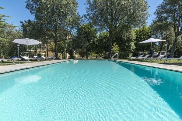A clear swimming pool with lounge chairs and umbrellas, surrounded by trees.