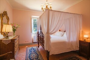 A bedroom with a four-poster bed, a chandelier, a dresser, and a nightstand.
