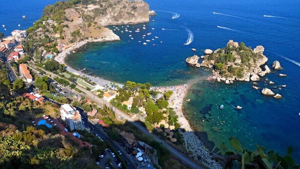 An aerial view of a coastal town with a beach, rocky outcrops, and boats in the water.