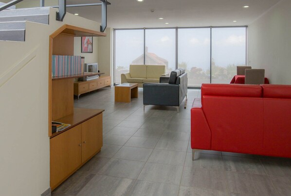 A modern living room with a staircase, a red sofa, a beige sofa, and a wooden cabinet with books.