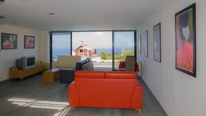 A modern living room with a large window, a red sofa, and a television on a wooden cabinet. - A Casa do Lagar In a peaceful and solitary area with a pleasant climate all year (São Jorge)