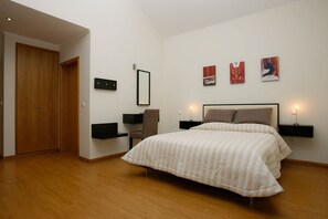 Un dormitorio con cama, mesitas de noche, una silla, armario y cuadros en la pared.