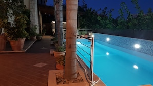 An outdoor swimming pool area with a tiled walkway, potted plants, and a metal railing.
