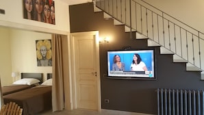 A hotel room with a bed, a TV mounted on the wall, a staircase, and artwork on the walls.