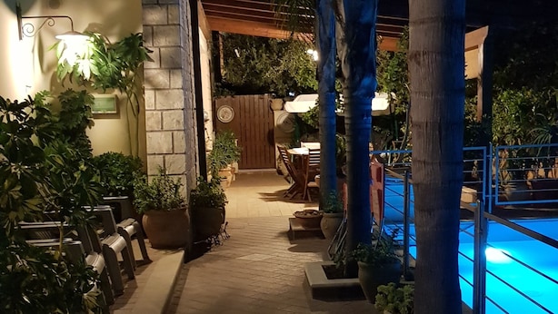 A nighttime outdoor area with a pool, potted plants, and a pathway leading to a wooden door.