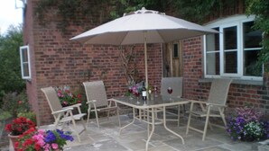 Une terrasse extérieure avec une table et des chaises, un grand parasol et des plantes en pot.