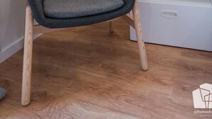 Een moderne stoel met houten poten en een grijs gestoffeerde zitting, geplaatst naast een witte nachtkastje met een lamp.