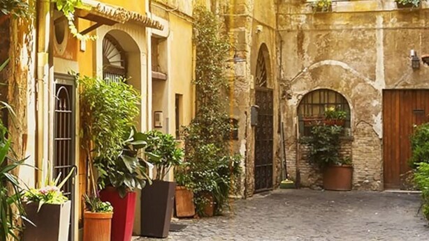 A narrow cobblestone street flanked by historic buildings with arched doorways and large potted plants. - Casa Camilla, new welcoming structure to feel at home (Roma)