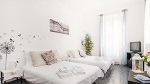 A hotel room with two beds, a television, a small table with a lamp, and a wall decoration. - Casa Camilla, new welcoming structure to feel at home (Roma)
