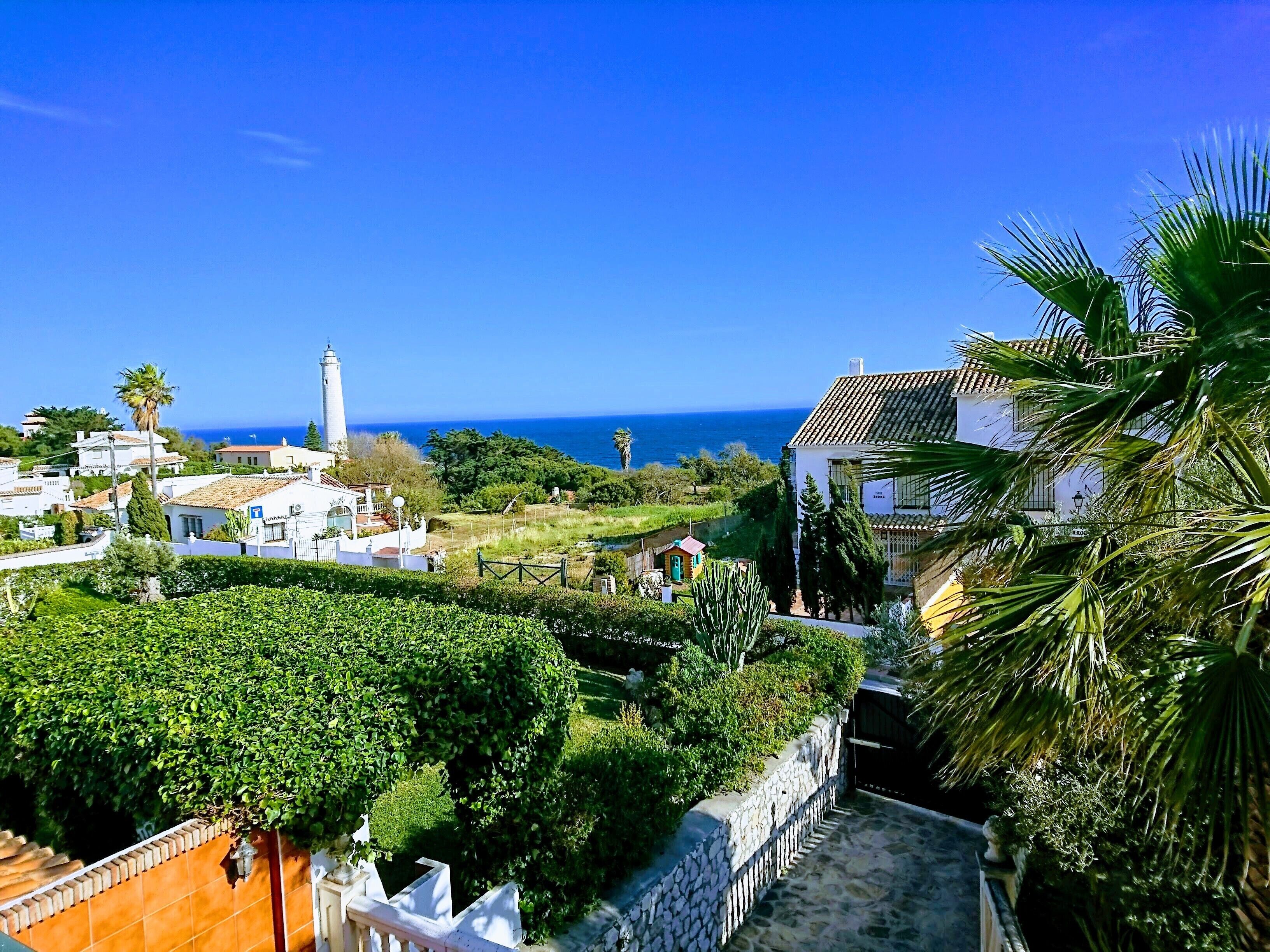 Uma vila costeira com um farol, edifícios brancos e vista para o mar.