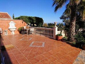 Une terrasse avec un sol carrelé, une balustrade blanche et une table entourée de chaises.