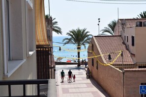 A coastal street with buildings, a beach, and people walking.