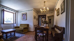 A living room with a sofa, a wooden coffee table, a dining table with chairs, a chandelier, and a cabinet with framed pictures. - Martina, apartment with terrace on the green hills of San Giminiano (San Gimignano)