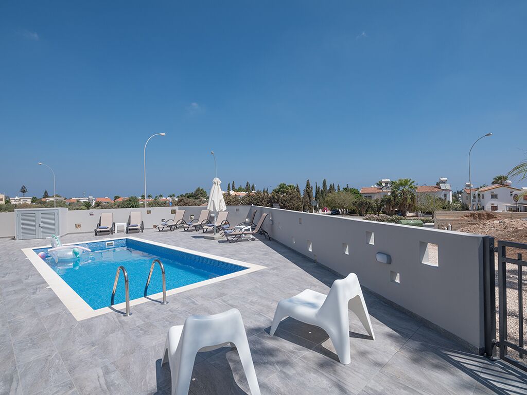 A rooftop pool area with a clear blue pool, white lounge chairs, and a view of the surrounding landscape.