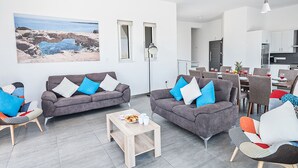 A modern living room with two grey sofas, a coffee table, and a dining area with chairs and a table. - Villa Desi, Luxury and new 5BDR Protaras Villa with pool and stunning sea views (Protaras)