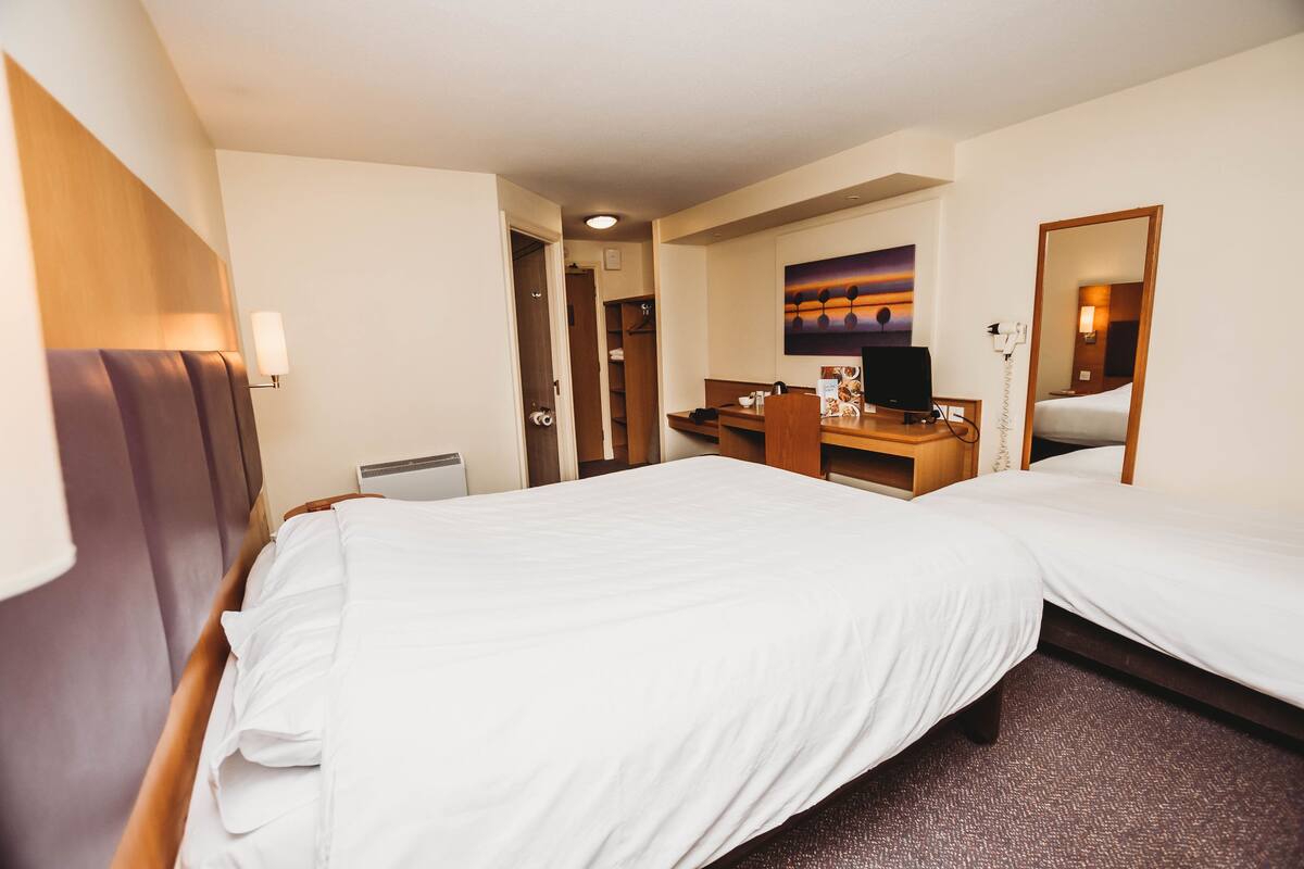 A hotel room with a large bed, a desk, a chair, a television, and a painting on the wall.