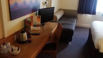 A hotel room with a wooden desk, a television, a sofa, a bed, and a painting on the wall.