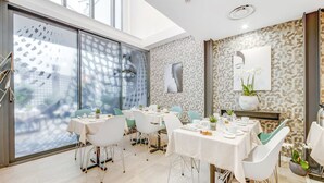 A modern dining area with white tables and chairs, a patterned wall, and a large window with a view of buildings.
