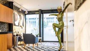 A statue of a dancer on a pedestal in a lobby with a checkered floor, a blue chair, and a wooden cabinet.