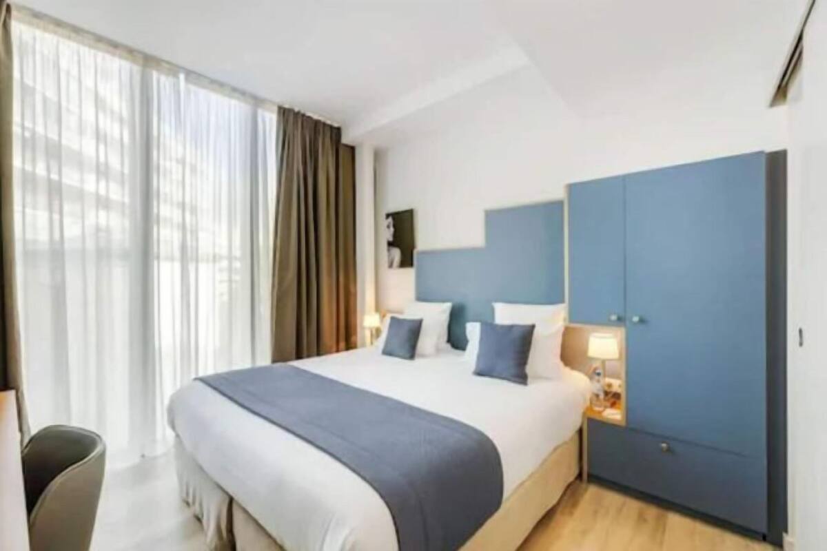 A hotel room with a large bed, a nightstand, a chair, and a wardrobe.