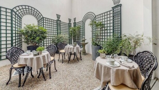 En indendørs patio med runde borde og stole, omgivet af grønne espalier og potteplanter.