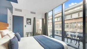 A modern hotel room with a large bed, a desk, and a balcony with outdoor seating.